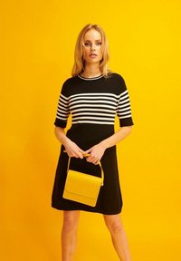 Mustavalkoiset raidalliset mekko, jossa on lyhyet hihat ja ribbikuvio, yhdistetty keltaiseen käsilaukkuun. Keltainen tausta.