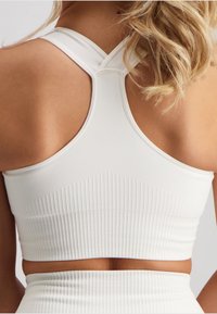 White sport bra with a ribbed texture. Crossed straps at the back and a fitted design. Smooth fabric with subtle detailing around the band.