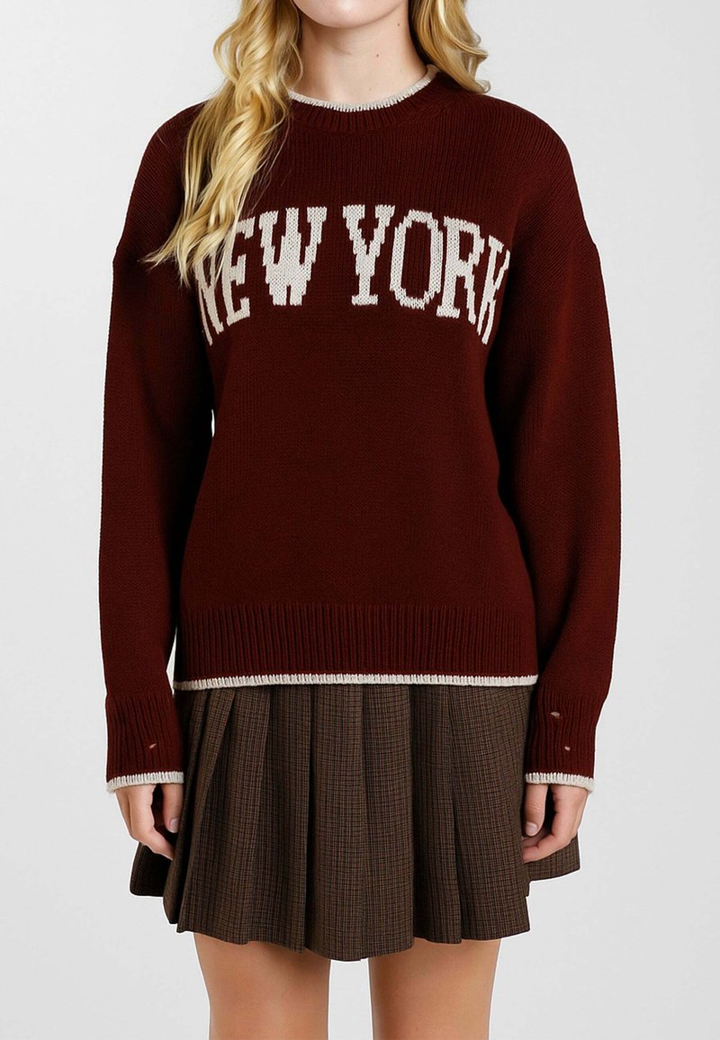 Maglione lavorato a maglia color mogano con la scritta "NEW YORK" in bianco, con scollo e polsini a coste, abbinato a una gonna plissettata marrone.