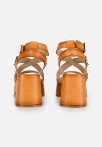 Brown leather high-heeled sandals featuring wide straps and a block heel. Open back with two adjustable buckles for fit.