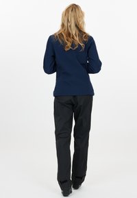 Marinblå softshell-jacka med långa ärmar och hög krage, tillsammans med svarta vattentäta byxor, lämplig för utomhusaktiviteter.