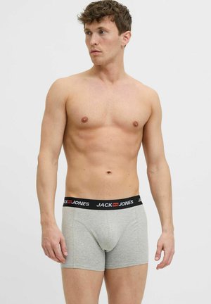 Grijze boxers met een zwarte tailleband waarop 'JACK & JONES' in het wit is gedrukt. De stof lijkt zacht en rekbaar. Model staat met een neutrale uitdrukking.
