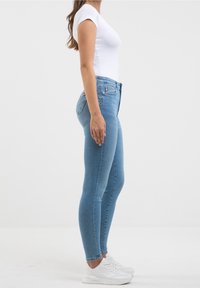 Jeans ajustados de color azul claro, hechos de mezclilla, con una cintura alta, un corte entallado y un ligero desgaste, con un estilo clásico de cinco bolsillos.