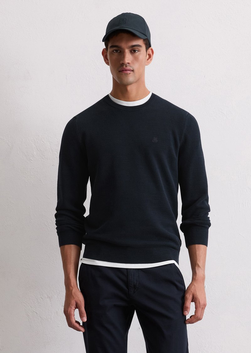 Pulover tricotat bleumarin cu un model texturat, guler rotund și margine albă. Asortat cu pantaloni închiși la culoare și o căciulă corespunzătoare.