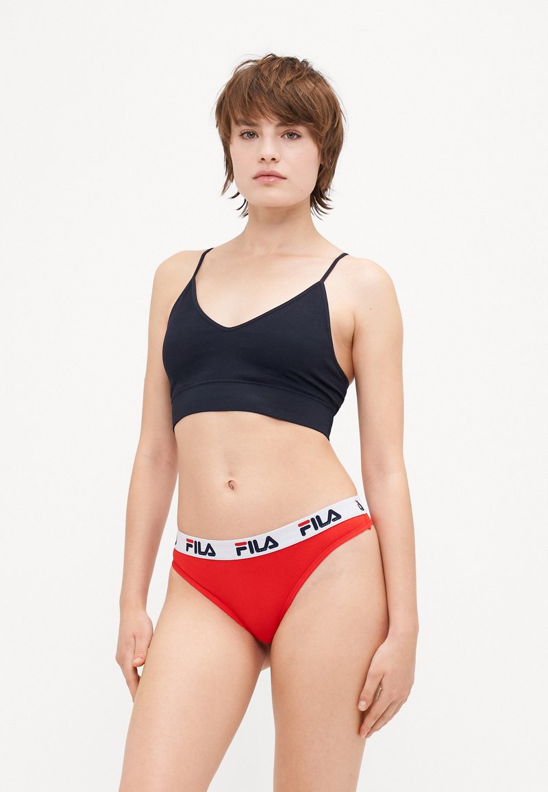 Svart rippet bralette med tynne stropper, parret med røde truser med hvit midjebånd med Fila-merke. Glatt stoff og tettsittende design.