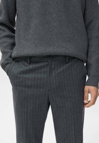 Maglione grigio a coste abbinato a pantaloni grigi a righe sottili. L'outfit presenta una vestibilità comoda e una sottile texture in tutto il capo.