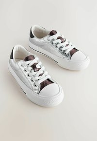 Srebrne sneakersy z fakturą skóry węża, z białymi sznurowadłami, białymi gumowymi czubkami i grubymi białymi podeszwami na neutralnym tle.