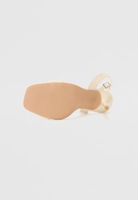 Beige høyhælte sandaler med en jevn, glatt finish, justerbar ankelrem og teksturert gummisåle for godt grep.
