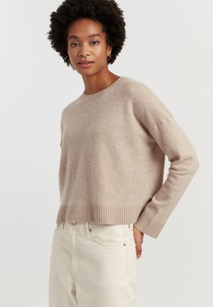 Maglione corto beige in morbido tessuto a maglia con scollo arrotondato e orlo a costine. Indossato con jeans bianchi off-white a vita alta, per un stile casual.
