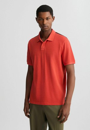 Polo shirt roșu cu mânecă scurtă, fabricat dintr-un material texturat, cu sistem de închidere cu trei butoane și un accent întunecat contrastant pe umeri.