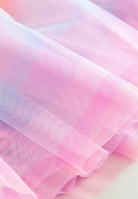 Tissu en maille rose doux plié avec un motif à fine grille et une texture semi-transparente visible à la lumière naturelle.