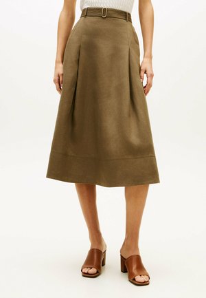 Frau trägt einen olivgrünen Midirock mit Falten und einem passenden Gürtel, kombiniert mit braunen offenem Zehenblockabsatz-Mules.