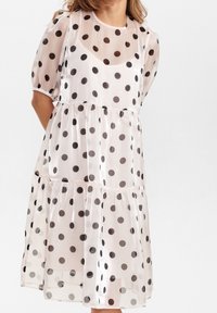 Genomskinlig, ljusrosa klänning med svarta prickar. Har korta puffärmar, rund halsringning och en lager-på-lager nederkant. Mjuk textur.