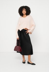 Ροζ ανοιχτόχρωμο πλεκτό κοντό πουλόβερ, μαύρη πλισέ midi φούστα, μαύρες μπαλαρίνες και μια μπορντό τσάντα χειρός με δομημένο σχέδιο.