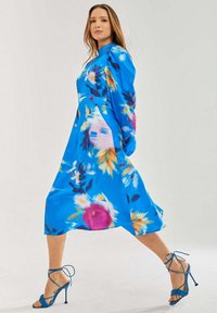 Blue floral dress with long sleeves and a flared skirt. Features colorful patterns and delicate floral accents. Paired with blue strappy heels.
