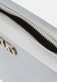 Pochette argentata con texture, dotata di una cerniera metallica e un accento logo. L'interno è nero, offrendo un contrasto elegante con l'esterno.