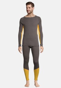 Grijs thermoshirt met lange mouwen en gele zijpanelen, gecombineerd met bijpassende grijze legging met gele accenten bij de enkels. Rekbaar materiaal en een getailleerd design.