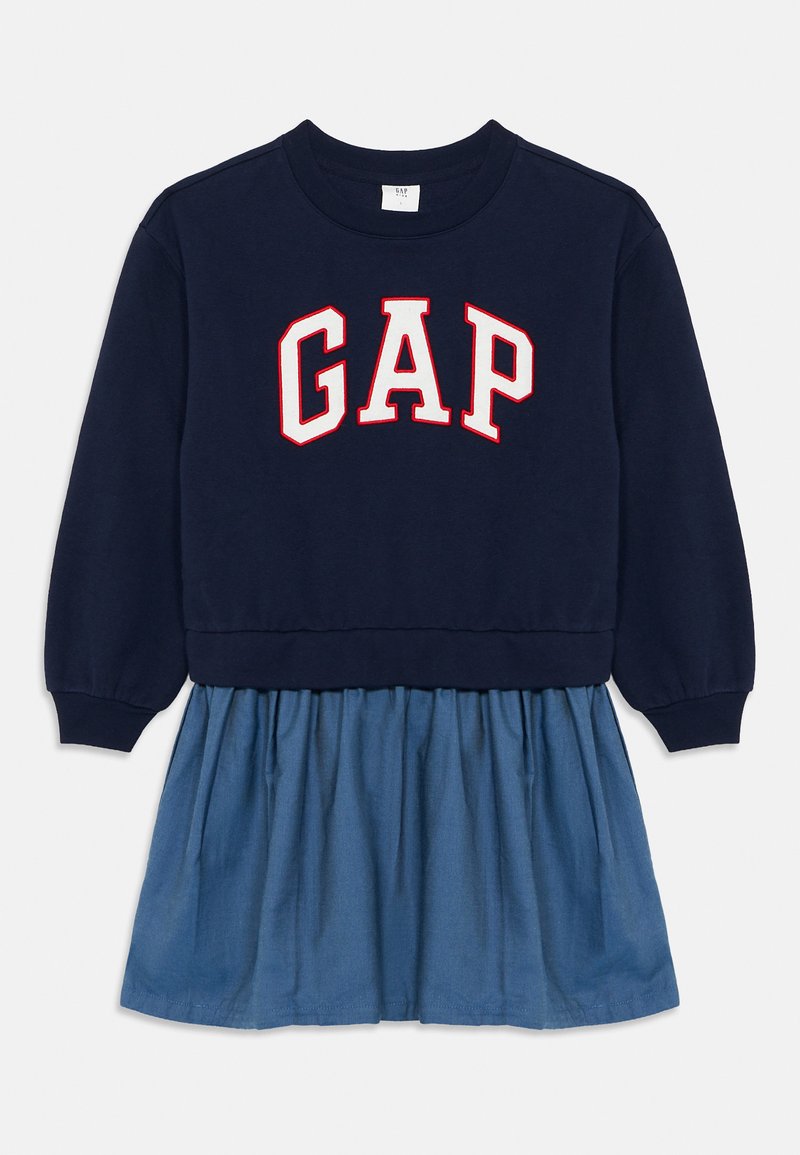 Sweatshirt bleumarin cu logo-ul roșu și alb "GAP", combinat cu o fustă din denim de culoare albastră deschisă. Prezintă manșete cu nervuri și un design de fustă plisată.