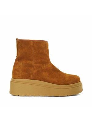 Bottine en suede marron avec une semelle en caoutchouc. Elle possède une languette et un bout arrondi. Accent en cuir lisse sur le bord supérieur.