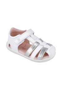 Sandalia blanca con tiras metálicas plateadas, diseño de punta abierta, correa ajustable de velcro, forro interior suave y pequeños cortes a los lados.