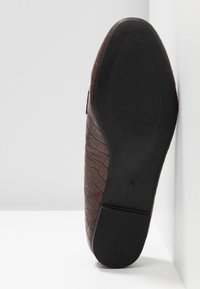 Chaussure habillée en cuir marron avec semelle texturée vue de dessous sur fond blanc.