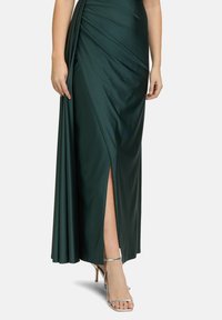 Langes, drapiertes Abendkleid aus dunkelgrünem Satin mit einem hohen Schlitz bis zum Oberschenkel, elegant geschnitten mit schönen Falten und akzentuiert durch metallische High Heels.