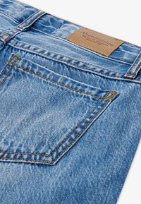 Tascone posteriore di jeans in denim blu chiaro con cuciture arancioni e una toppa in pelle marrone etichettata Abercrombie.