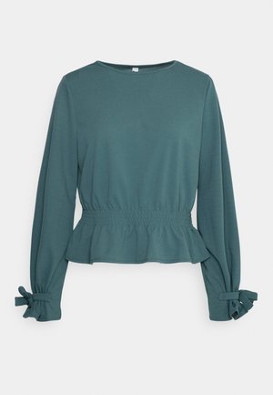 Blusa de manga larga color azul verdoso con cintura elástica fruncida, bajo con peplum, escote redondo y lazos atados en cada puño.