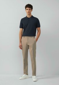 Marineblaues Poloshirt mit Dreiknopfleiste, beigefarbene maßgeschneiderte Hose und weiße Sneaker. Glatte Stofftextur mit klassischer Passform.
