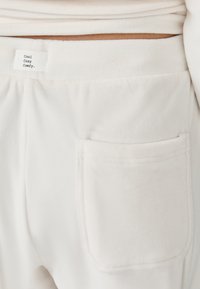 Des joggers en polaire blanche présentent une poche cousue et une étiquette indiquant "Cool Cozy Comfy". Texture douce et taille élastique pour le confort.