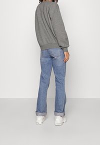 Šedá mikina s žebrovanými manžetami, spárovaná se světle modrými dżínami rovného střihu. Džínsy mají ohrnuté manžety, a celý outfit doplňují bílé tenisky.