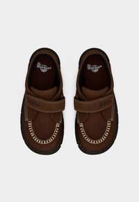 Καφέ δερμάτινα παπούτσια παιδικά Dr. Martens με ιμάντες hook-and-loop, λευκά ράμματα και μαύρες λαστιχένιες σόλες σε λευκό φόντο.