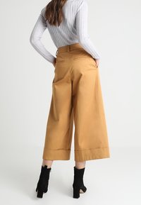 Beiga vida byxor med pressveck, hög midja och bakfickor, kombinerade med svarta högklackade ankelboots.