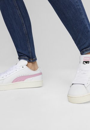 Adidași albi cu o dungă roz pe lateral, talpă din cauciuc texturat și limbă căptușită. Purtați cu blugi de culoare albastră închis.