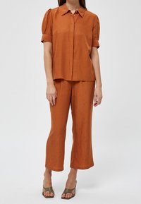 Rust-colored blouse with short puff sleeves, buttoned front, paired with matching wide-leg pants featuring a subtle pattern. Smooth texture.