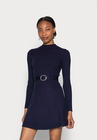 Marineblaues langärmliges Kleid mit hohem Kragen, tailliertem Oberteil und ausgestelltem Rock. Verfügt über einen breiten Gürtel mit einer runden Metall-Schnalle. Glatte Textur.