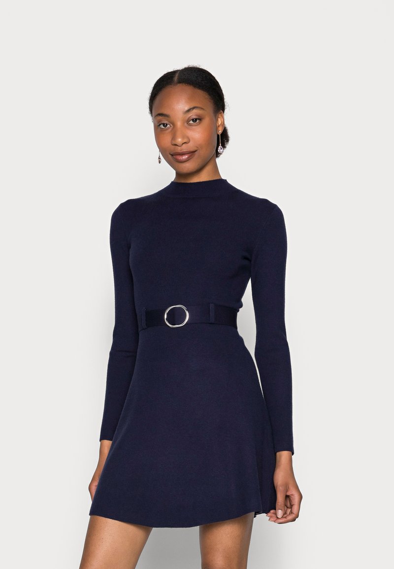 Marineblaues langärmliges Kleid mit hohem Kragen, tailliertem Oberteil und ausgestelltem Rock. Verfügt über einen breiten Gürtel mit einer runden Metall-Schnalle. Glatte Textur.