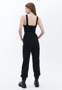 Top corto negro ajustado con tirantes anchos y espalda descubierta, combinado con pantalones cargo negros de cintura elástica y botas negras gruesas.