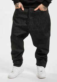 Black denim pants with a relaxed fit, featuring side pockets and a straight leg cut, paired with white athletic sneakers.