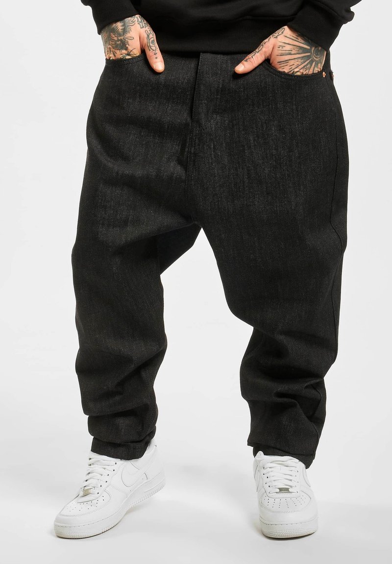 Black denim pants with a relaxed fit, featuring side pockets and a straight leg cut, paired with white athletic sneakers.