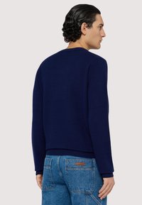 Marinblå stickad tröja med lång ärm, ribbad halsringning och ärmslut, matchad med ljusblå denimjeans med en lapp på bakfickan.