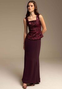 Top peplum burdeos con textura intrincada, combinado con una falda larga y ajustada en un tono profundo a juego. La modelo se encuentra en un entorno neutro.