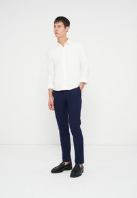 Camicia bianca a maniche lunghe con bottoni, pantaloni slim-fit blu navy e mocassini neri. Tessuto liscio con una morbida texture; design casual e aderente.