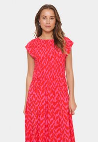 Robe à motifs rouges et roses avec des manches volantées, taille smockée et jupe fluide. Fabriquée en tissu léger pour le confort.