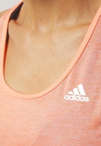 Peachfarvet atletisk tank top med rund halsudskæring, lavet af letvægtsstof, med et hvidt Adidas-logo på venstre brystområde.