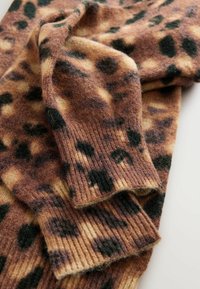 Pull en tricot doux plié avec un motif léopard marron, beige et noir, montrant des poignets côtelés et un gros plan sur le tissu texturé.