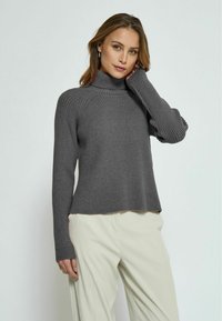 Gray knitted sweater with a high neck, ribbed texture, and long sleeves; paired with light beige trousers, displayed against a neutral background.