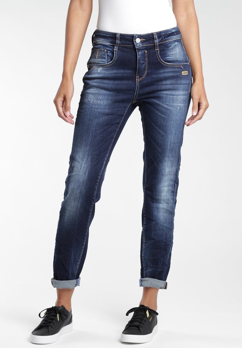 Mörkblå denimjeans med en blekt finish, med uppvikta muddar och femficksdesign. Bärs med svarta sneakers, vilket visar en avslappnad look.