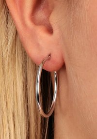 Orecchino a cerchio in argento, design circolare, finitura metallica lucida, di dimensioni medie, fissato tramite un lobo dell'orecchio forato con bordi lisci.