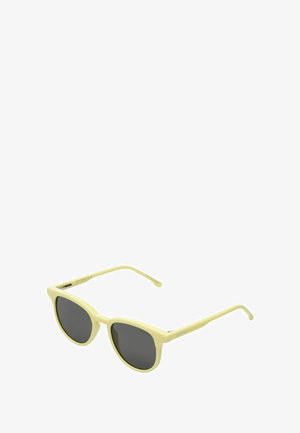 Lunettes de soleil teintées jaunes avec des verres ronds, teinte des verres gris foncé et fines branches. Design minimaliste avec une finition mate.